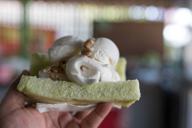 Close up of coconut ice creams on pandan leaf bread with roasted peanuts on top in man hand. Thai style ice cream.