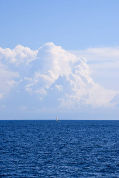 Scenic view of clouds over the sea and a distant sailboat on the horizon
