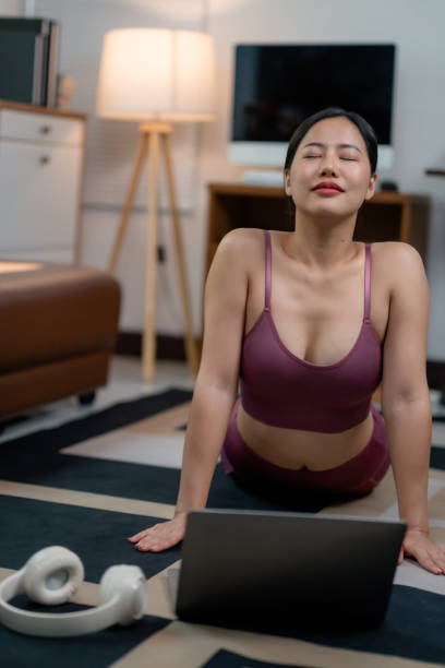 istock Young Asian woman practicing yoga via laptop tutorial, stretching on floor mat, engaging in home workout, embodying wellness lifestyle 2201500020