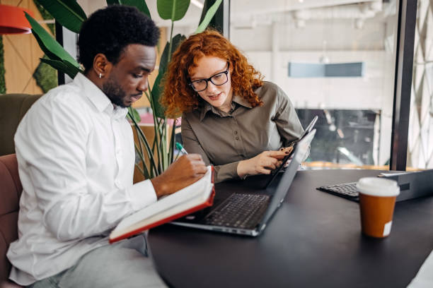 istock Two young adults working together in office while sitting in front of laptop 2201500797