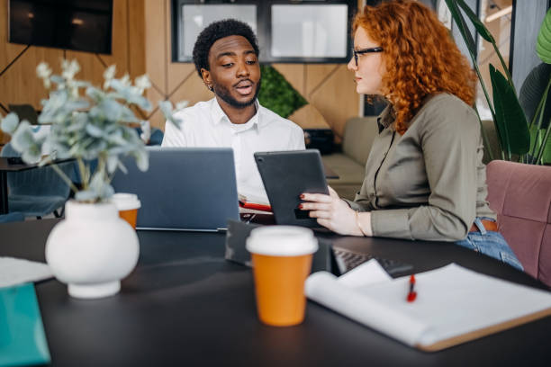 istock Two young adults working together in office while looking at laptop tablet 2201500811