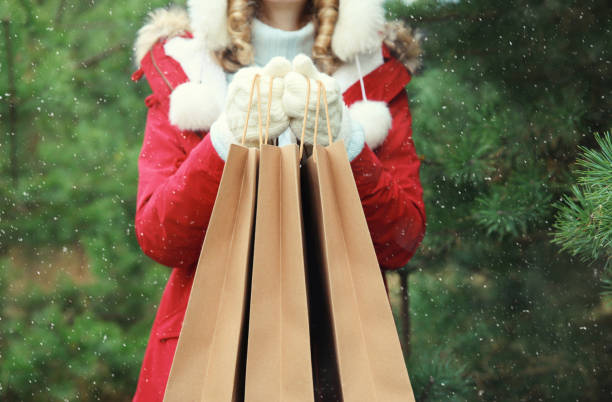 Purchase, holidays, female hand holding showing paper shopping bags, gift against Christmas tree stock photo