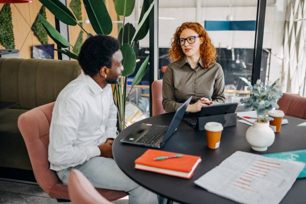 istock Two young adults working together in office and having discussion while sitting in front of laptop and digital tablet 2201501178