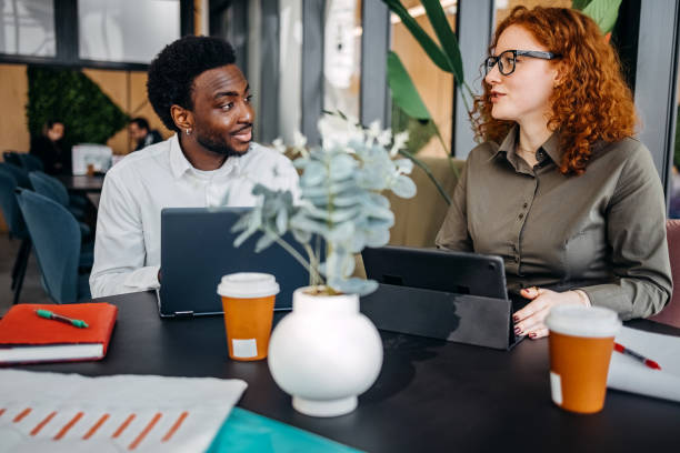istock Two young adults working together in office and having discussion while sitting in front of laptop and digital tablet 2201501215