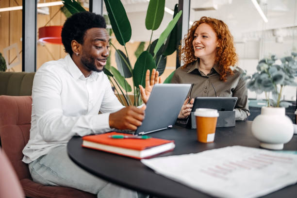 istock Two young adults working together in office and having discussion while sitting in front of laptop and digital tablet 2201501253