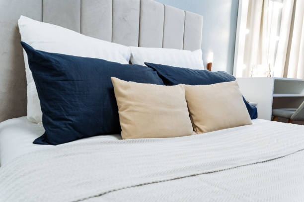 istock In a cozy bedroom, there is a lovely bed adorned with crisp white sheets, complemented beautifully by blue and tan pillows, creating a serene and inviting atmosphere for relaxation 2201519158