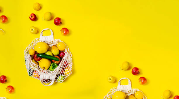 White string bag with different vegetables and fruits on a yellow background. top view