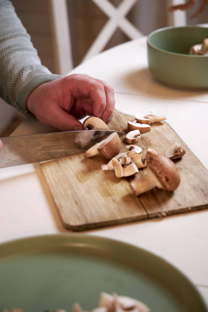 istock man cuts mushrooms on a wooden board on the kitchen table , close-up 2201522959