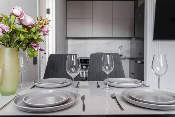 istock modern kitchen design with built-in furniture. In foreground is kitchen table with serving. plates, glasses, and vase of pink flowers on table. Stylish kitchen in shades of grey. 2201525387