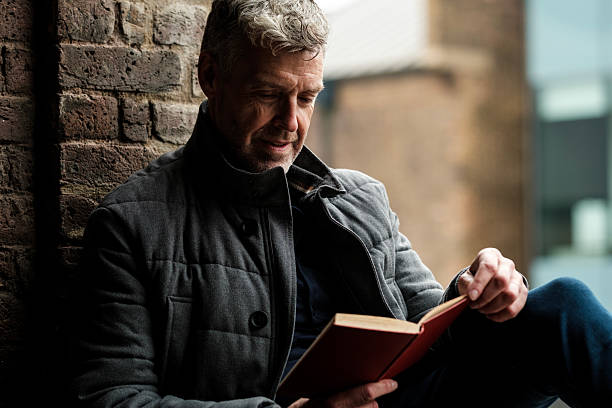 istock Grey-haired man reading a book enjoying his free time 2201525441