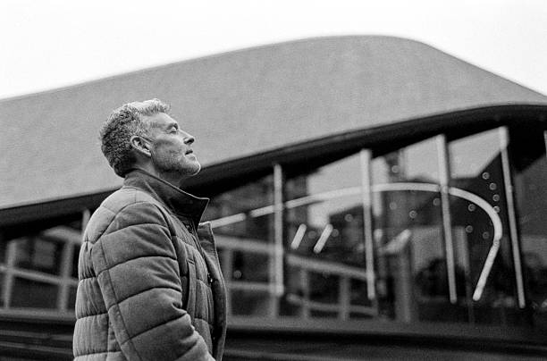 istock Mature man wearing winter jacket observing modern architecture in monochrome analog style 2201525475