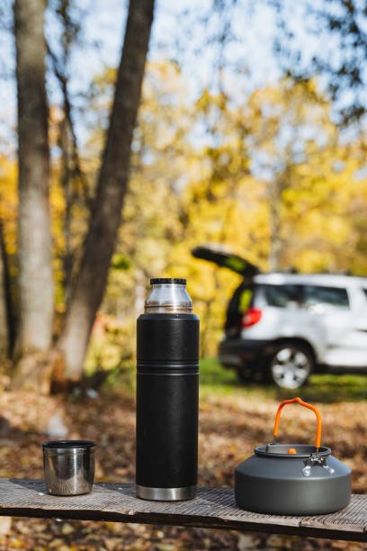 A shiny black thermos rests gracefully beside a charming tea kettle on a beautifully crafted wooden table, enhancing the elegance and warmth of this inviting and cozy setting