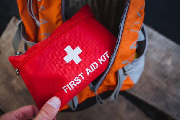 istock A person is holding a standard first aid kit directly in front of an orange backpack, which is likely used for travel or outdoor activities, showing preparedness and safety awareness 2201525630