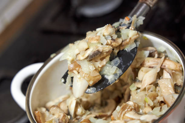 fried mushrooms with onions lying in an enameled white pot, close-up view from above