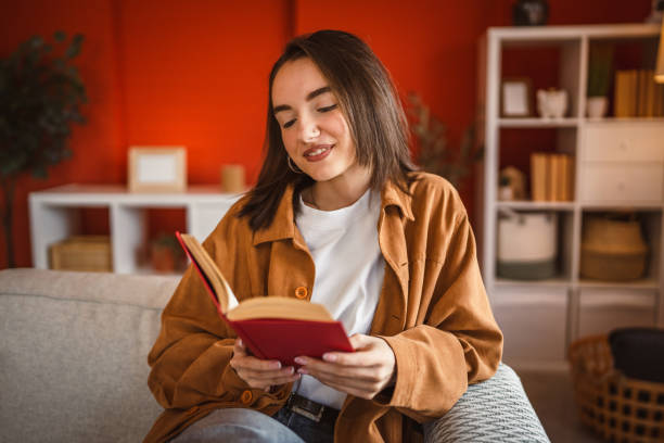 istock beautiful young woman enjoy and smile while read a book at home 2201534465