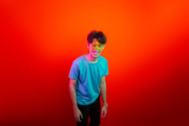 istock Handsome young man wearing carnival mask and looking at camera. Happy and fun. Isolated on orange neon background. 2201542329