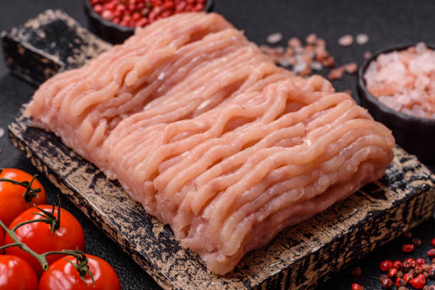 Raw minced chicken with salt, spices and herbs on a dark concrete background