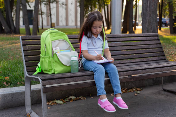 istock Young girl studying outdoors on park bench with backpack 2201546626