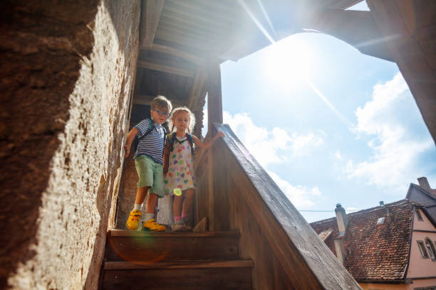 A boy and a girl walk down a wooden stairway in Rothenburg ob der Tauber, with the sun shining brightly above rooftops