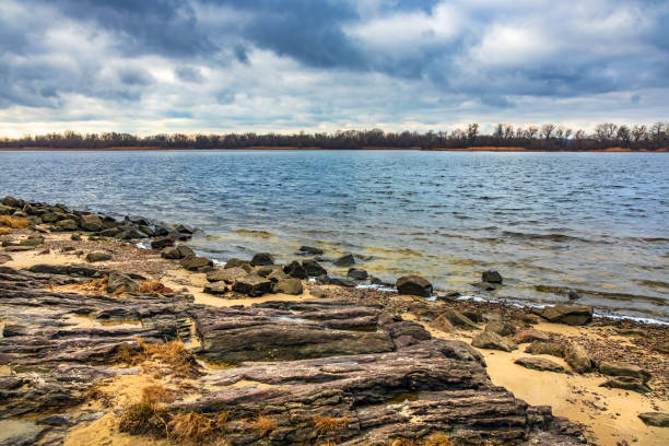 Wide river, cloudy day. Stones and sand on the shore, waves on the water, and clouds in the sky. Landscape with the Dnieper River