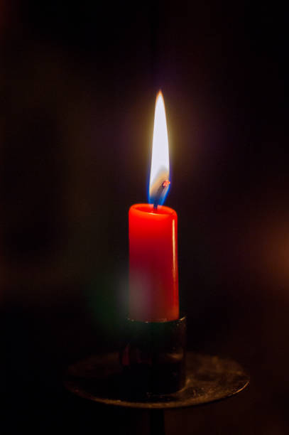 red candle burning in darkness with soft glow.