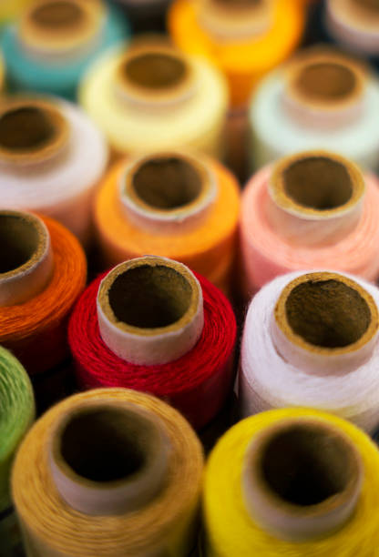 A detailed close-up shot of colorful thread reels, placed alongside a reel, on a white background. Ideal for emphasizing details in crafting or sewing projects.