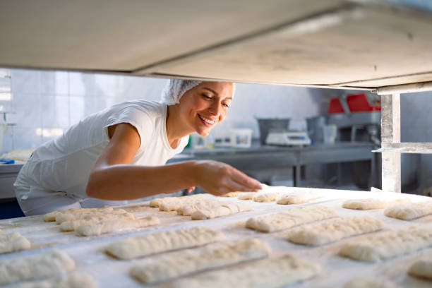 istock Baker arranging loaves of bread on a baking sheet in a bakery 2201565856