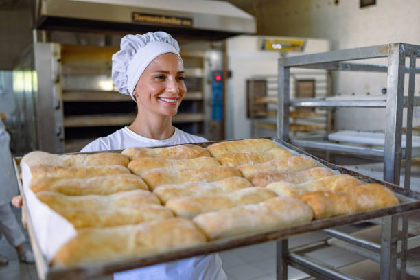 istock Baker smiling and holding a tray of freshly baked bread in a bakery 2201565940