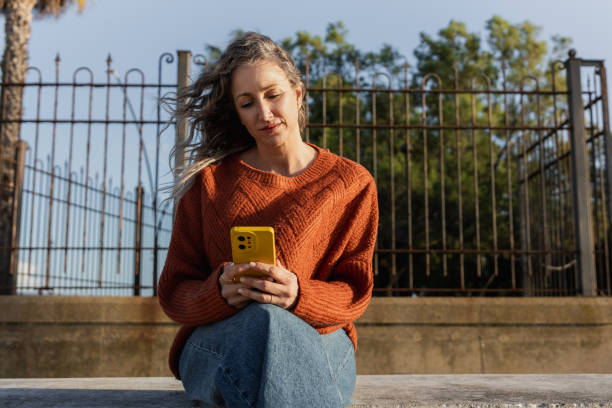 istock Mid adult woman using smartphone while sitting outdoors 2201570332