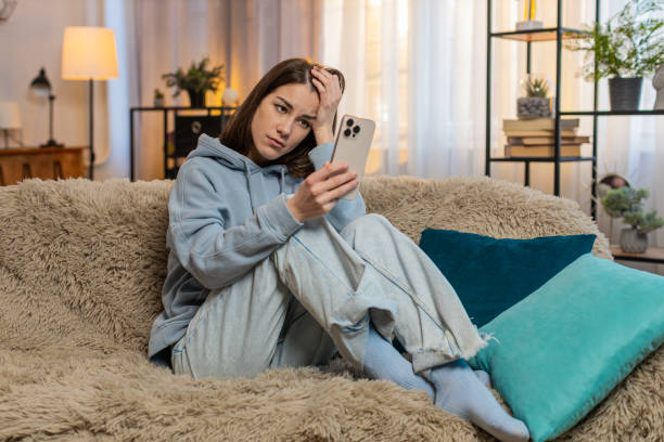 istock Young woman on sofa using smartphone expressing deep disappointment due to bad news or losing a game 2201571794