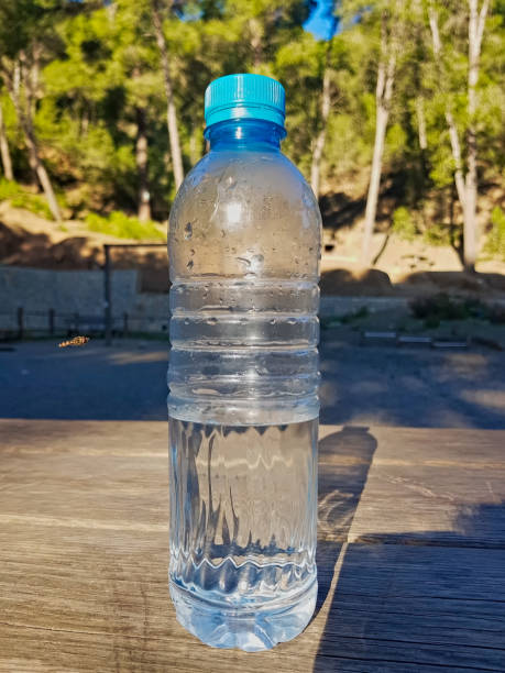 istock A plastic water bottle, filled halfway, rests on a wooden surface, where sunlight and shadows play 2201576554