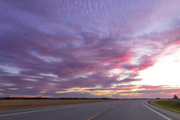 Spectacular purple and pink sunset in prairies with cloudy sky over the highway through the countryside.