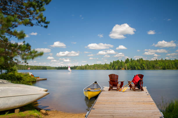 istock Adirondack chairs on a dock, yellow canoe, others on the shore. 2201609352