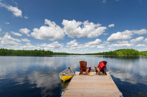 istock Adirondack chairs on a dock, yellow canoe floating nearby. 2201609364