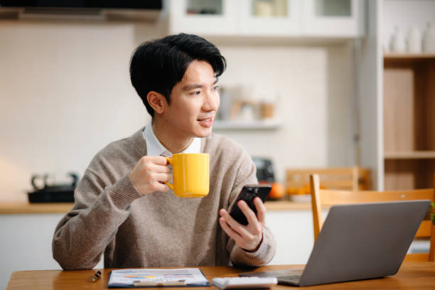 istock Young Asian man with sitting working on laptops and tablets in a cozy workspace. Perfect for education, innovation, and remote work themes 2201611546