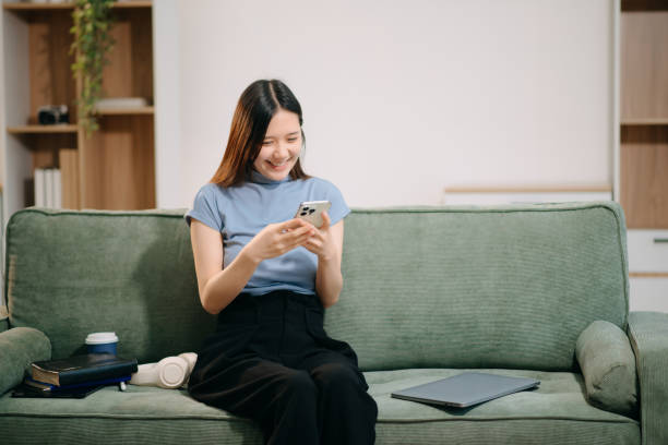 istock Young asian woman using smartphone and tablet while seated on couch at home 2201611651