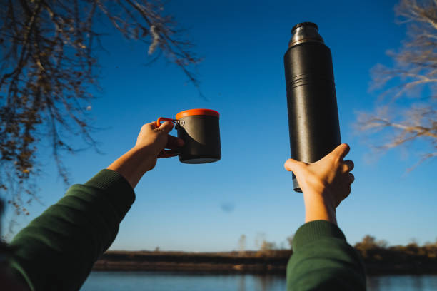 istock A person is seen holding a cup filled with a warm beverage in one hand, while clutching a thermos of a hot drink in the other, savoring a beautiful day outdoors, immersed in nature 2201619410