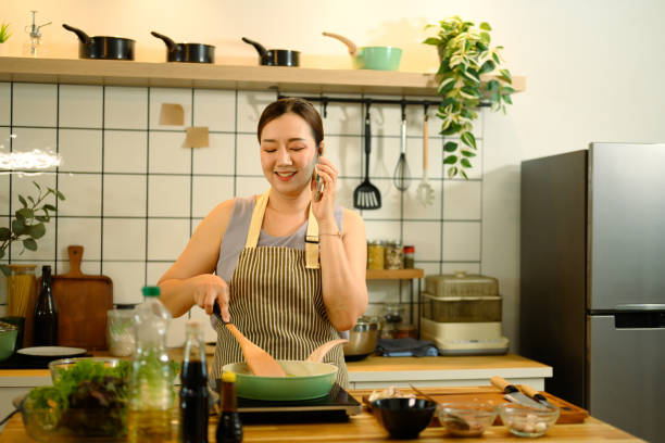 istock Smiling middle aged woman in apron cooking and talking on mobile phone in a kitchen 2201624683