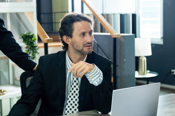 istock Businessman sitting at a desk in a modern office, discussing project while focusing on a laptop screen. Professional environment representing corporate planning, decision-making, and teamwork success. 2201626156