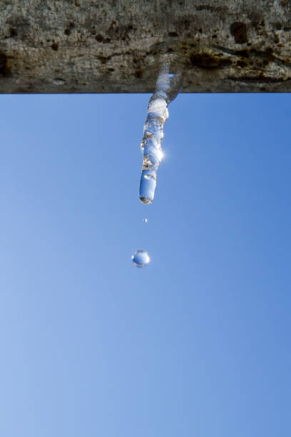 Spring icicle with a drop of water against a blue sky. Weighty drops.