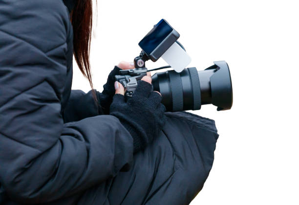 A woman is holding a camera with a blue lens. She is wearing a black jacket and gloves
