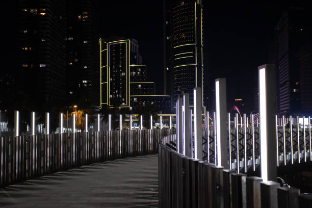 Nighttime cityscape featuring illuminated urban architecture, bright decorative lights, and a modern pedestrian bridge creating a futuristic ambiance.