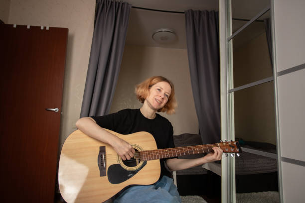 istock Woman Practicing Guitar in Cozy Bedroom, learning music through chords and strumming, engaged in skill-building indoors. 2201631785