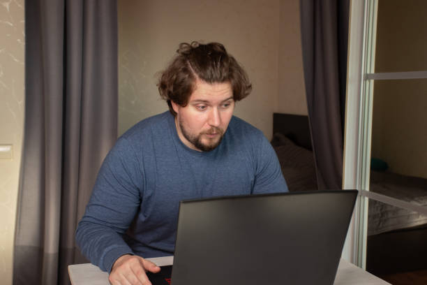 istock Surprised man at laptop, navigating a modern workspace, intrigued by technology and internet 2201631787