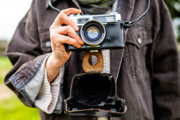 istock Photographer is holding a vintage camera outdoors, with the camera case open and hanging below, suggesting a moment of preparation or anticipation for taking a photograph 2201631837