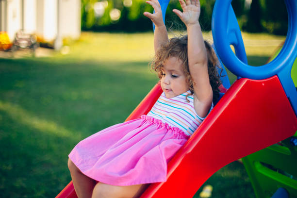Little girl sliding down a slide in her backyard playground