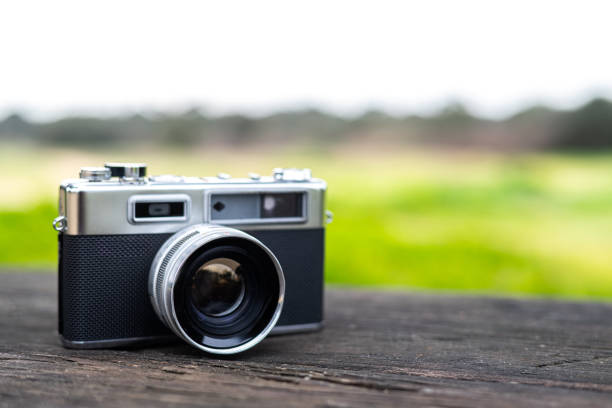 istock Classic analog camera sits on a weathered wooden surface, its lens reflecting the blurred greenery of the background, evoking a sense of nostalgia and timeless photography 2201632055