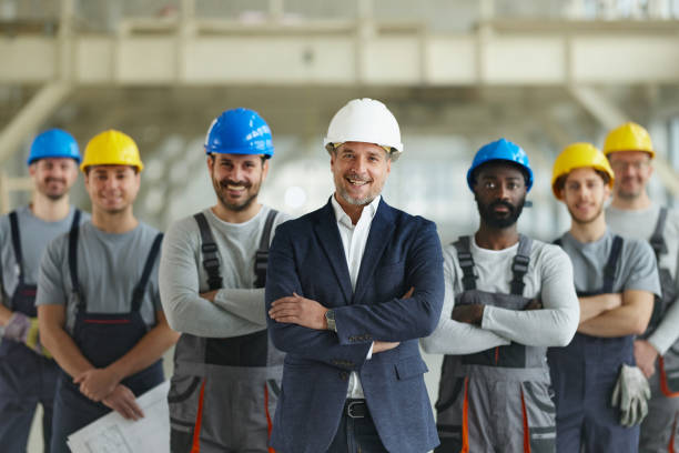 istock Happy architect in front of team of manual workers at construction site. 2201635069