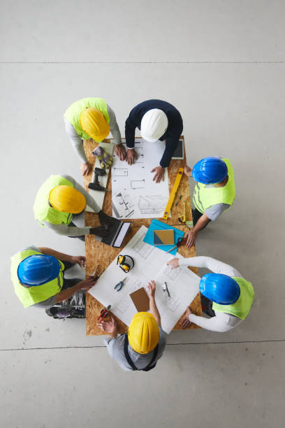 Above view of architect and manual workers working on plans at construction site.