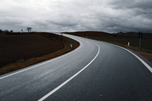 Curving road in the Tuscan countryside under dark storm clouds. The wet pavement and rolling hills create a dramatic and atmospheric landscape